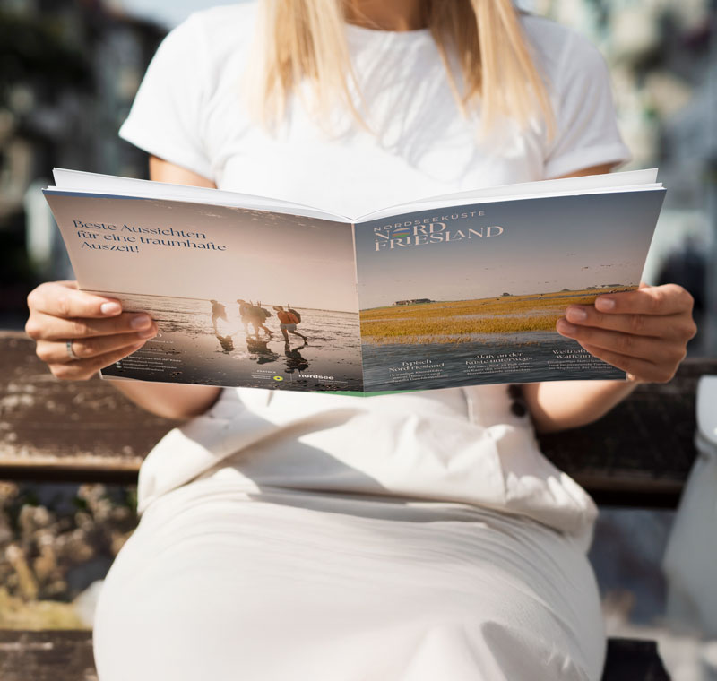Eine Person blättert im Urlaubsmagazin der Nordseeküste Nordfriesland.