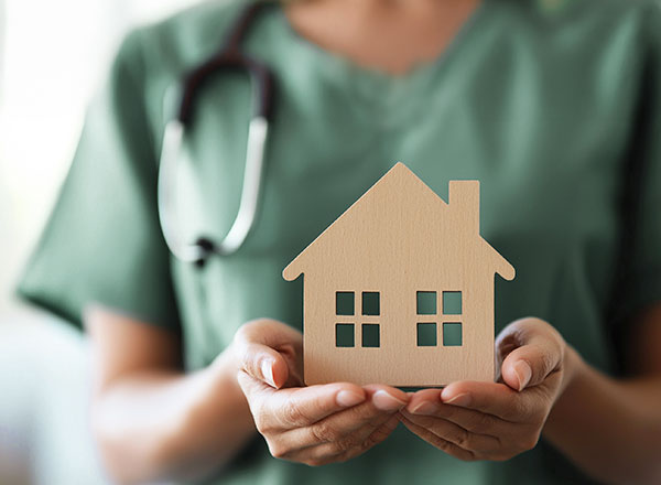 Hände halten ein hölzernes Häusschen.