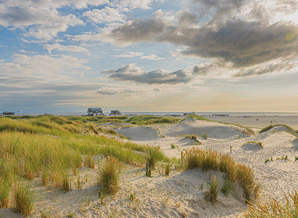 Ein Blick auf die Dünen und einen entfernten Pfahlbau in St. Peter-Ording.