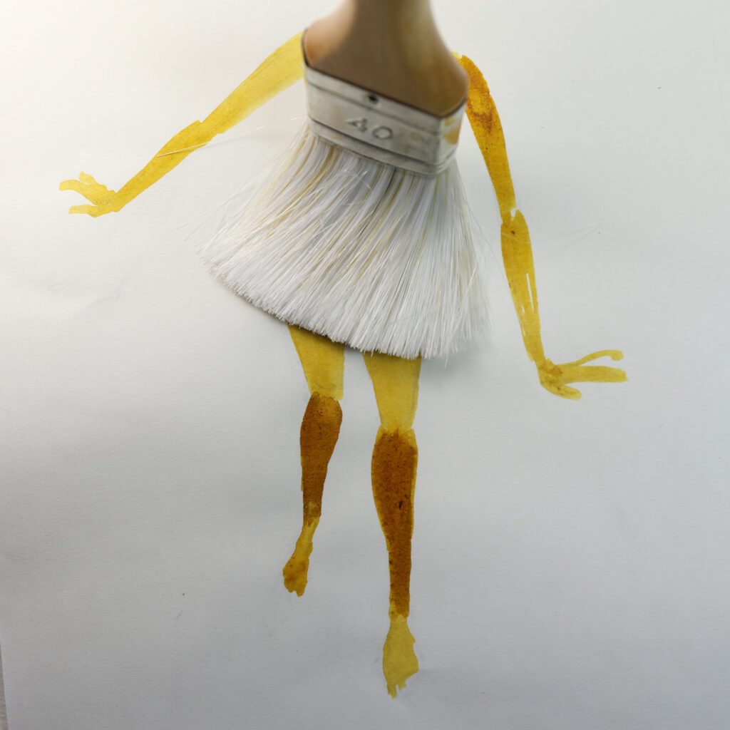 Ein aufs Papier gedrückter Pinsel dient als Kleid eines gemalten Mädchens.